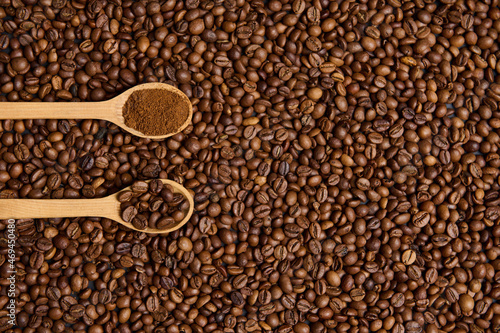 Top view of wooden spoons with ground coffee and roasted coffee beans on the background of scattered fresh roasted coffee grains with copy space for advertisement. Flat lay composition