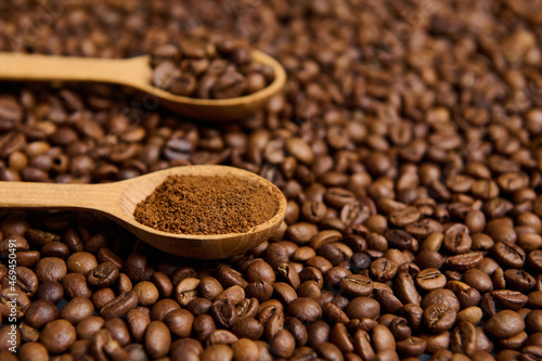 Close-up of wooden spoons with ground coffee and roasted coffee beans on the background of scattered fresh roasted coffee grains with copy space for advertisement.
