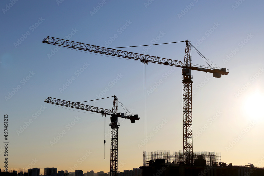 Silhouettes of two tower cranes and buildings under construction on sunrise background. Housing construction, apartment block in city