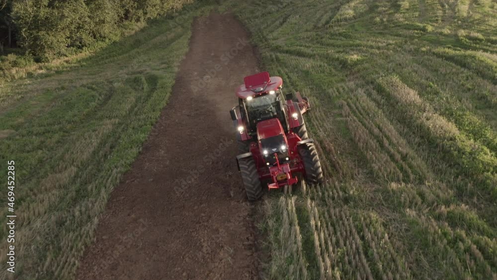 A modern tractor plows the land in a green field at sunset A modern tractor plows the land in a green field at sunset