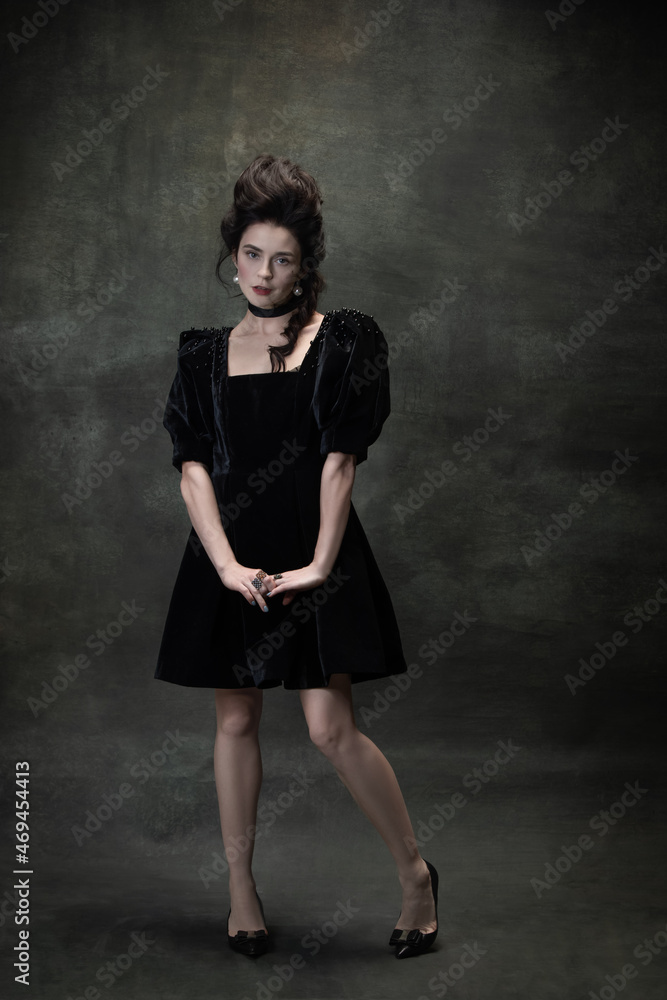 Classic retro portrait of young beautiful woman in image of medieval royal person in black dress isolated on dark vintage background.