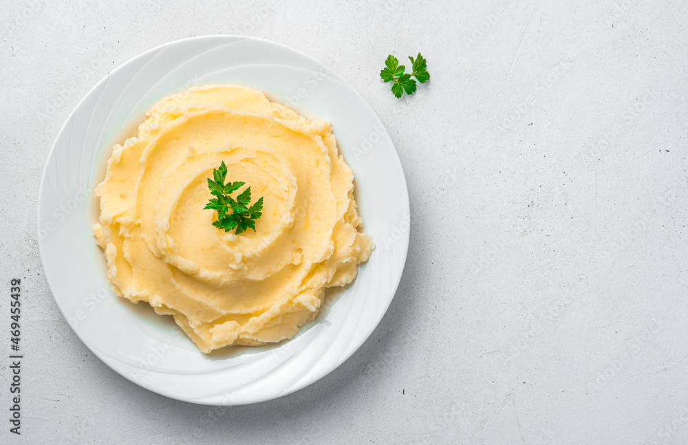 Mashed potatoes with basil in a white plate on a gray background.