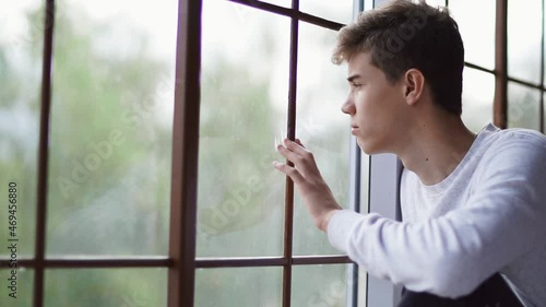 A young teenager looks out the window with a sad look. Isolated. Self-isolation.