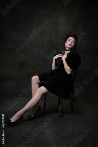 Classic retro portrait of young adorable woman in image of medieval royal person in black dress isolated on dark vintage background. © master1305