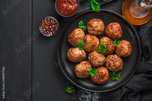 Fried meatballs with basil in a black plate on a dark background.