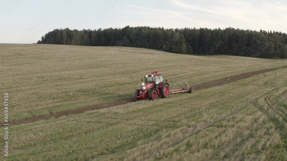 A modern tractor plows the land in a green field at sunset A modern tractor plows the land in a green field at sunset