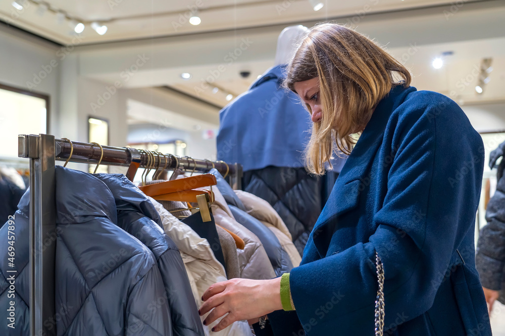 Obraz premium Portrait of happy woman customer chooses jacket in clothing store. Customer making choices in shop with clothes