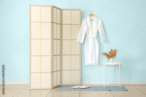 Folding screen, bathrobe and table with vase near blue wall