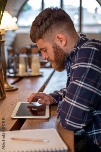 Freelancer dressed in casual outfit focus on reading news and looking on digital tablet while sitting in cozy urban cafe. photo
