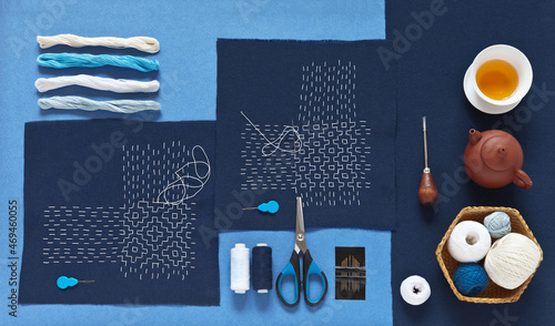 Foto Top view of two hand-made Sashiko embroidery in Japanese style, different types of threads, blue cotton fabrics, scissors, needles and green tea on blue background