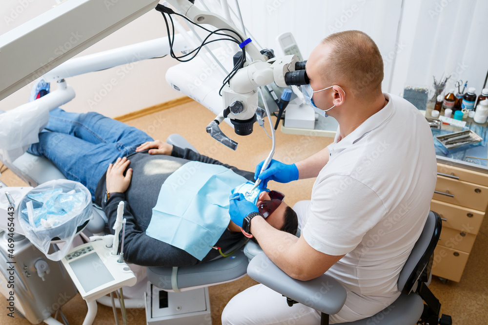The dentist treats his patient's teeth with a microscope. The dentist treats the patient's mouth. Dental care The dentist treats his patient's teeth with a microscope. The dentist treats the patient's mouth. Dental care