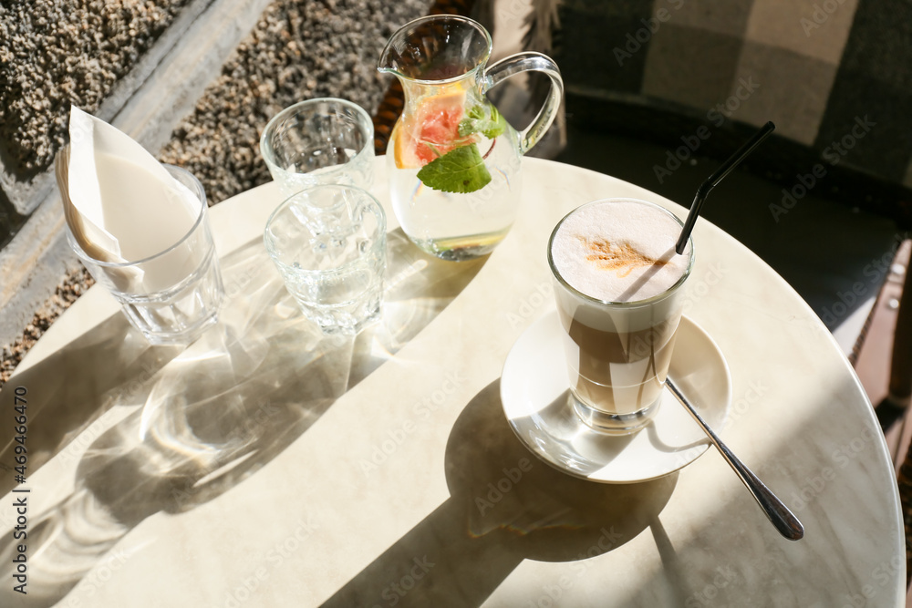 Glass of tasty coffee and jug with water on table in outdoor cafe