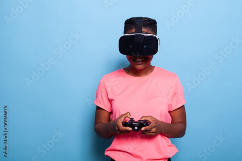 Portrait of african american young woman player wearing virtual reality headset playing space shoother video games using gaming joystick standing in studio with blue background. Videogames concept photo