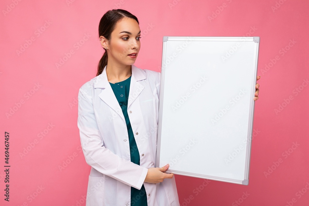 Female person doctor in a white medical coat holding blank board with copy space for text isolated on pink background. Epidemic concept Female person doctor in a white medical coat holding blank board with copy space for text isolated on pink background. Epidemic concept