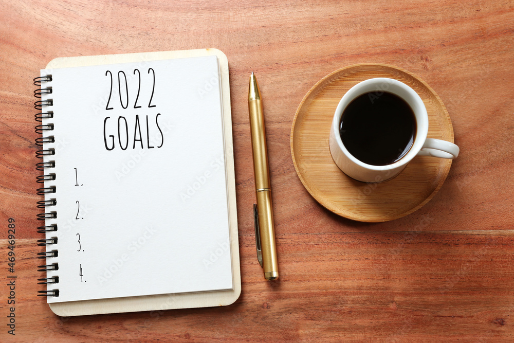 Business concept of top view 2022 goals list with notebook, cup of coffee over wooden desk Business concept of top view 2022 goals list with notebook, cup of coffee over wooden desk