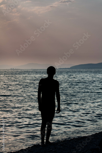 Contemporary art dramatic portrait silhouette a man at the sea in rays of the setting sun against the backdrop dark waves and beautiful evening sky