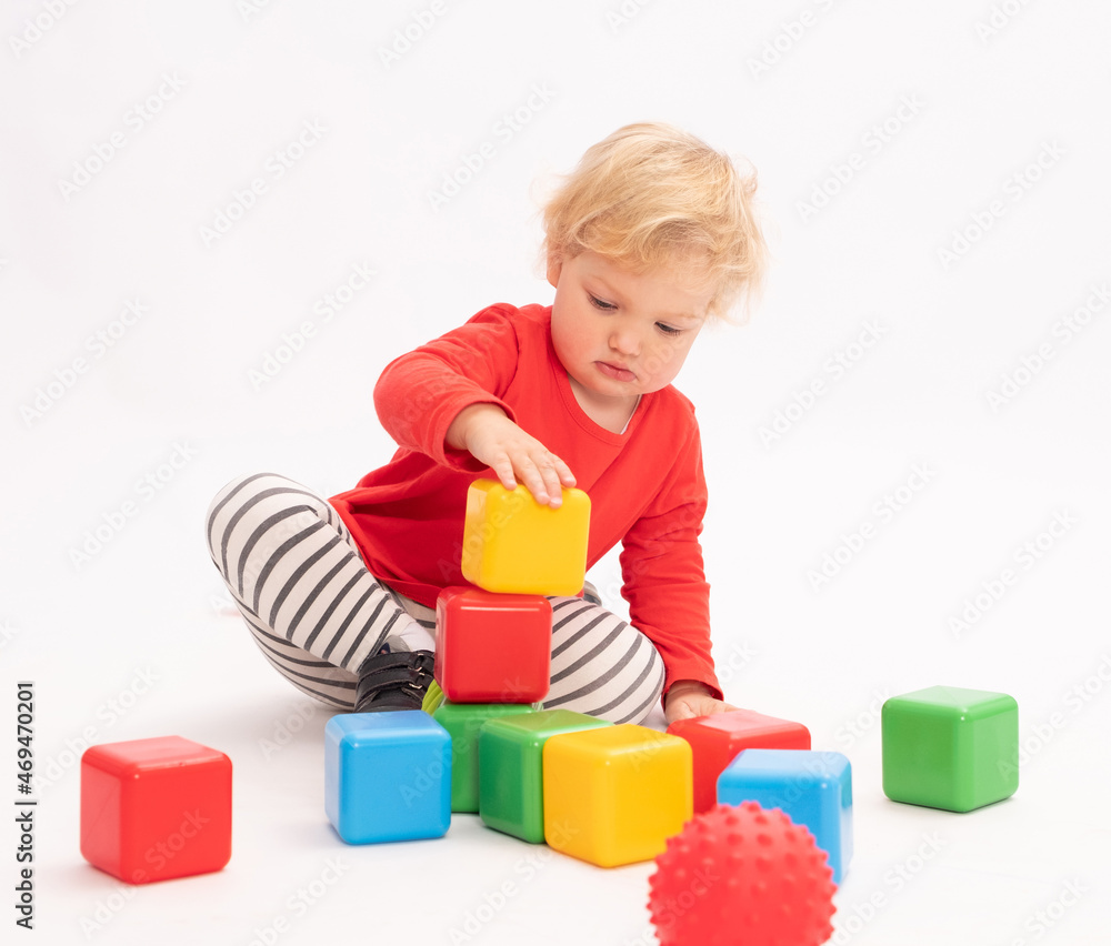 Cute little girl is building a tower from colorful cubes, white background Cute little girl is building a tower from colorful cubes, white background