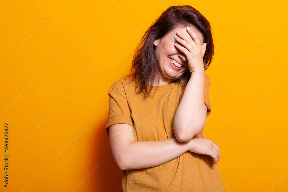 Portrait of woman smiling while covering eyes and face in studio. Positive adult using hand to hide from camera, feeling shy and laughing, standing over isolated background. Careful person Portrait of woman smiling while covering eyes and face in studio. Positive adult using hand to hide from camera, feeling shy and laughing, standing over isolated background. Careful person