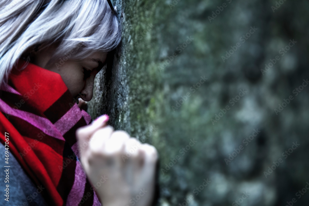 Conceptual image: hopelessness, depression, anxiety and frustration. Stressed  woman leans on the wall.  She punches with fists on cold stone wall.