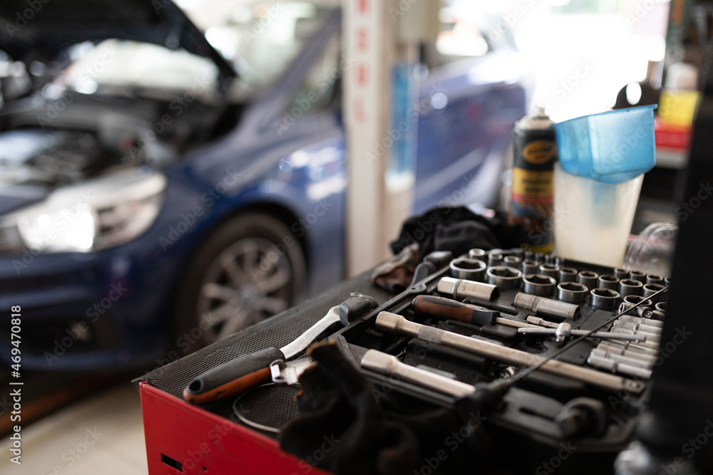 Obraz premium Photo of a set of tools against the background of a blue passenger car at a service station under repair with an open hood