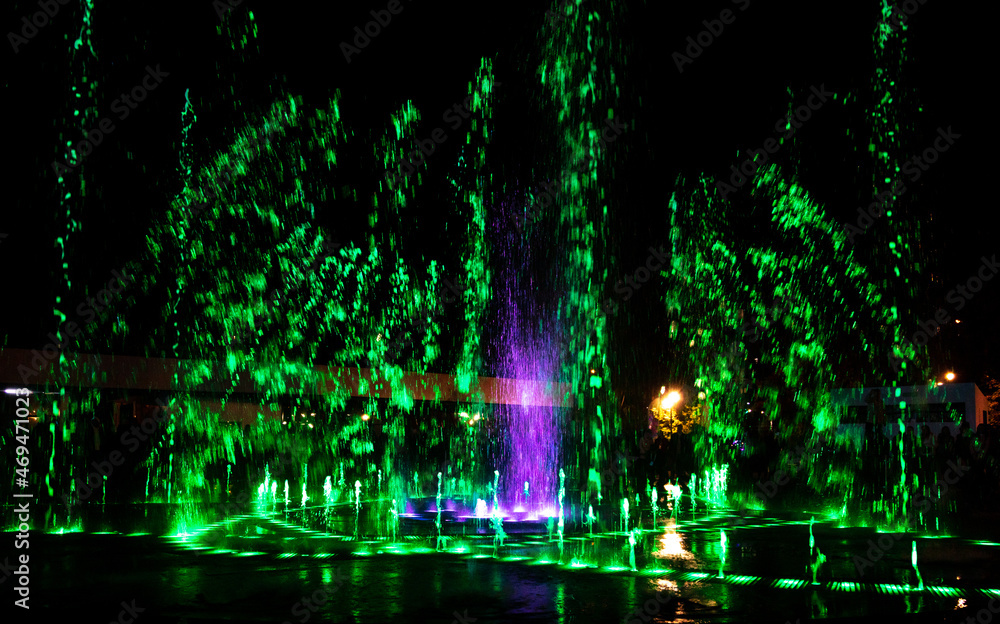 Green-pink jets of the fountain at night.