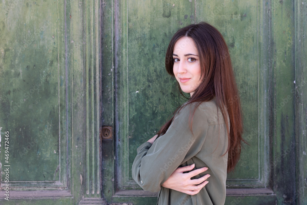 Fototapeta premium Young Brunette stylish lady posing in a green old door background