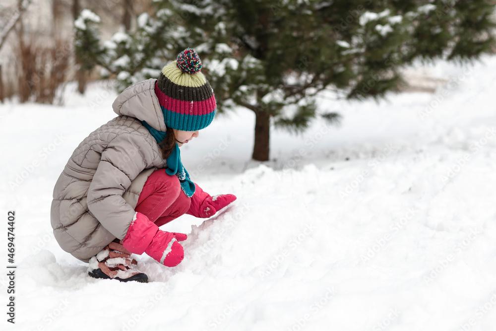 Playing in the snow. The girl kid child in warm waterproof winter suit in waterproof mittens plays in the snow outside 