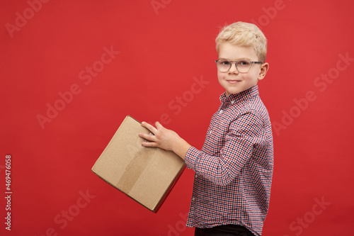 Delivery of goods and gifts project. Smiling boy with box on red background