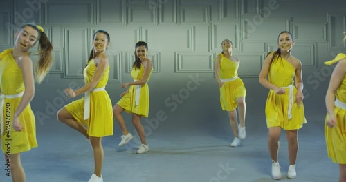 4k Group of beautiful , funny, stylish girls in yellow dresses dancing inside pavilion with grey background  . Synchronized dance of female ensemble for video clip  Woman dancers with the same outfit 