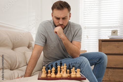 Thoughtful young man playing chess alone on sofa at home