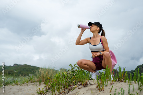 Fototapeta Naklejka Na Ścianę i Meble -  Sporty fit woman taking a rest for drinking water on outdoor fitness and running workout at the beach. Asturias coast, Spain.
