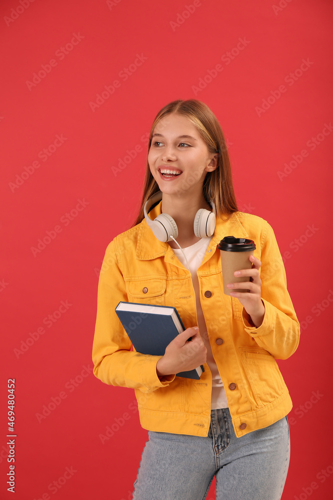 Teenage student with book, cup of coffee and headphones on red background Teenage student with book, cup of coffee and headphones on red background