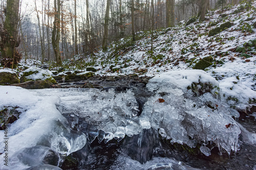 Freezing stream. Ice crystals over flowing water. Winter morning in the forest