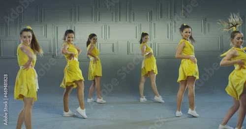 4k Group of beautiful , funny, stylish girls in yellow dresses dancing inside pavilion with grey background  . Synchronized dance of female ensemble for video clip  Woman dancers with the same outfit 