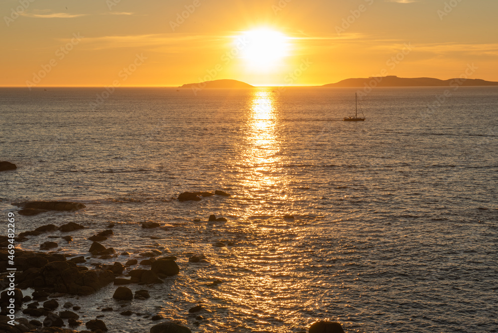sunset with a sailing boat with the Cies Islands and reflections of the sun on the sea