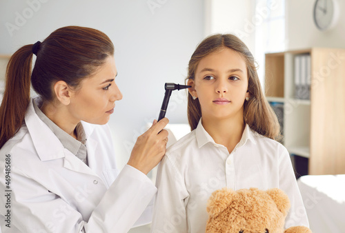 Child with teddy bear getting ENT examination in exam room at medical checkup at doctor's office. Female otolaryngologist holding otoscope and examining little kid's ear to prescribe the right therapy photo