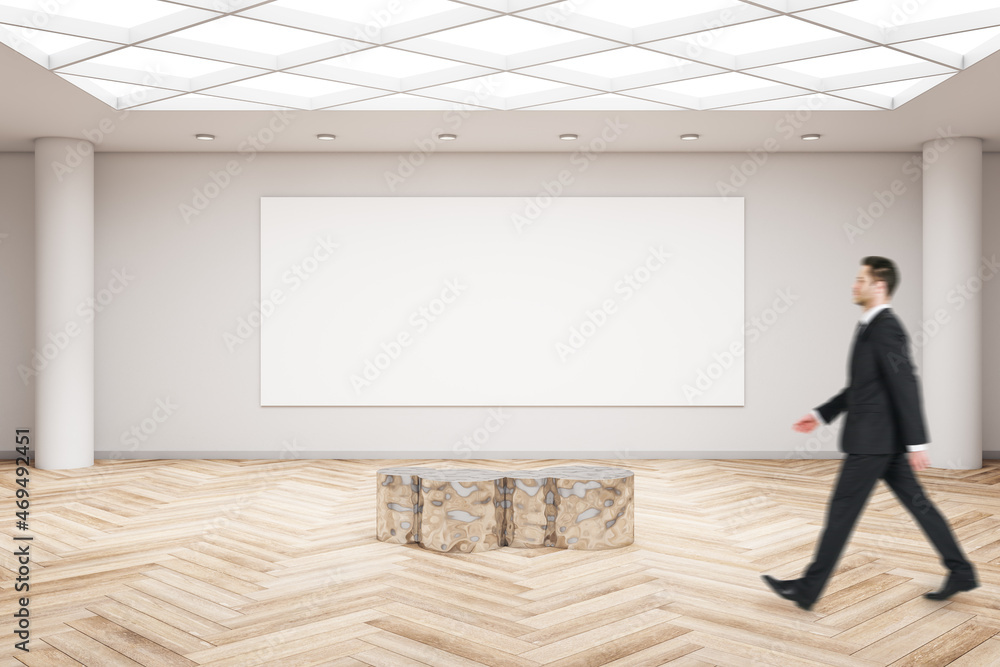 Businessman walking in modern exhibition hall interior with wooden flooring, shiny golden seat and empty mock up poster on concrete wall. Gallery and art concept.