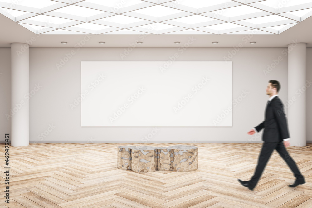 Businessman walking in modern exhibition hall interior with wooden flooring, shiny golden seat and empty mock up poster on concrete wall. Gallery and art concept. Businessman walking in modern exhibition hall interior with wooden flooring, shiny golden seat and empty mock up poster on concrete wall. Gallery and art concept.