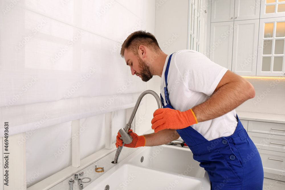 Professional plumber repairing water tap in kitchen