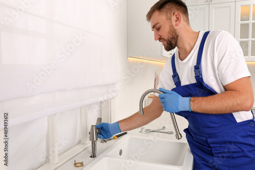 Professional plumber repairing water tap in kitchen