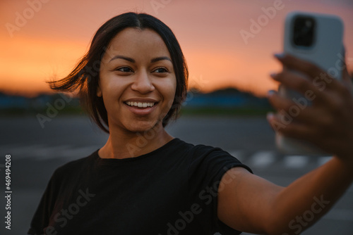 Black young woman in t-shirt smiling and taking selfie on cellphone