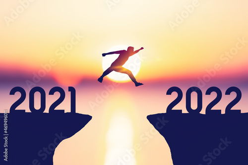 Silhouette man jumping between cliff with number 2021 to 2022 at tropical sunset beach. Freedom challenge and travel adventure holiday concept.