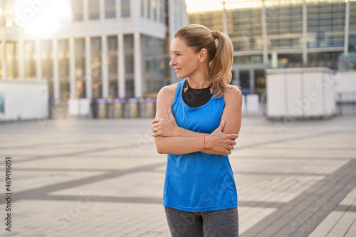 Beautiful middle aged woman in sportswear looking aside while standing outdoors, ready for workout in the city © Kostiantyn