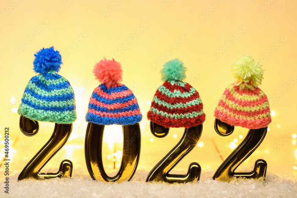 Gold numbers 2022 with multi-colored knitted hats on yellow background. New year backdrop with 2022 year