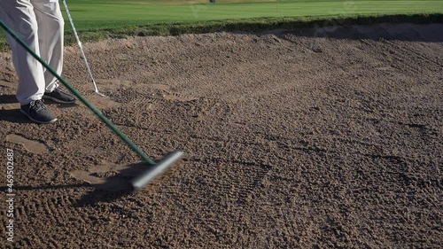 A man raking a bunker or sand trap at a golf course