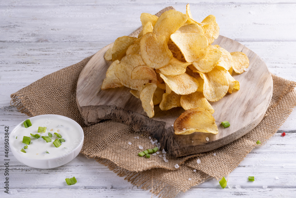 Delicious golden potato chips on a white wooden background.