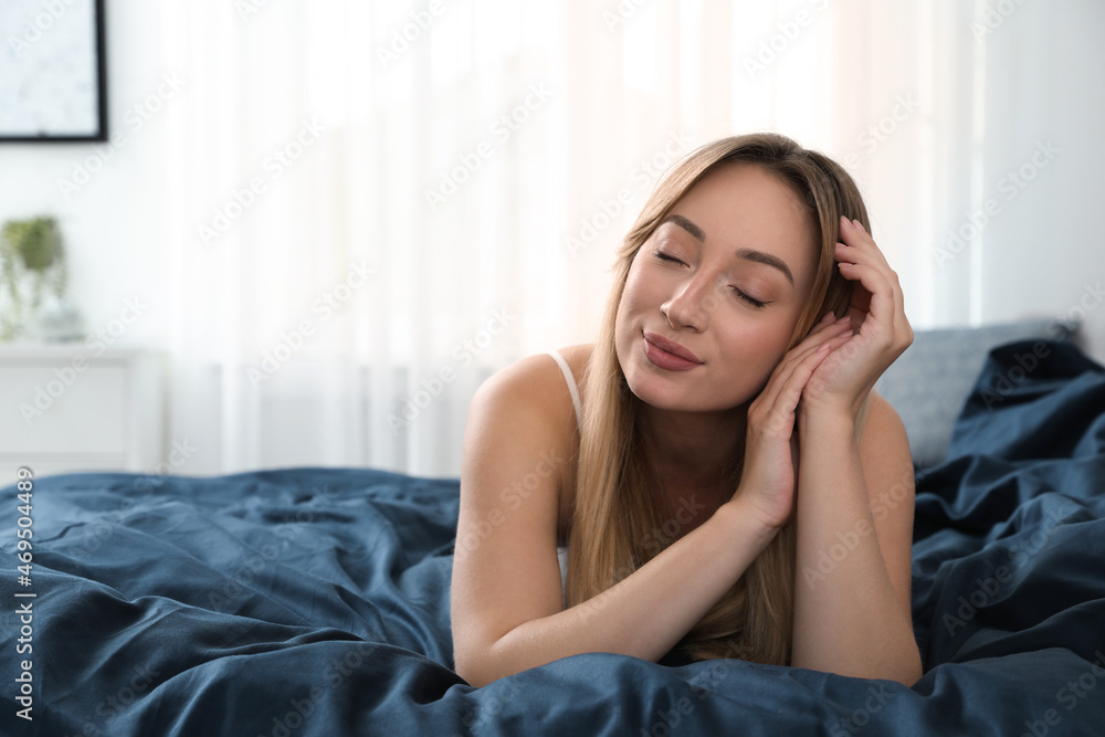 Young woman lying on comfortable bed with dark blue linens at home Young woman lying on comfortable bed with dark blue linens at home