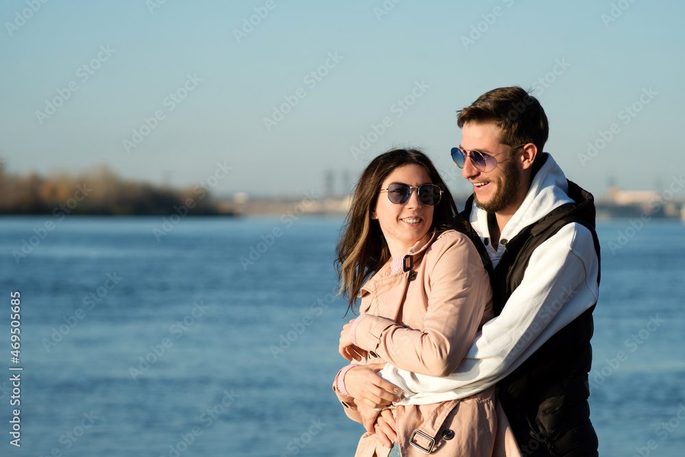 Happy young lovers stand enjoy vacation by sea beach. Lovely hipster couple hugging and having fun together outdoors. Concept of youth, love and lifestyle. Freeluft aesthetics. Casual style Happy young lovers stand enjoy vacation by sea beach. Lovely hipster couple hugging and having fun together outdoors. Concept of youth, love and lifestyle. Freeluft aesthetics. Casual style