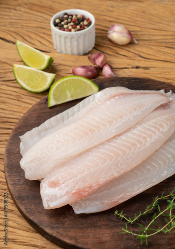 Raw tilapia fish fillet with seasonings over wooden table