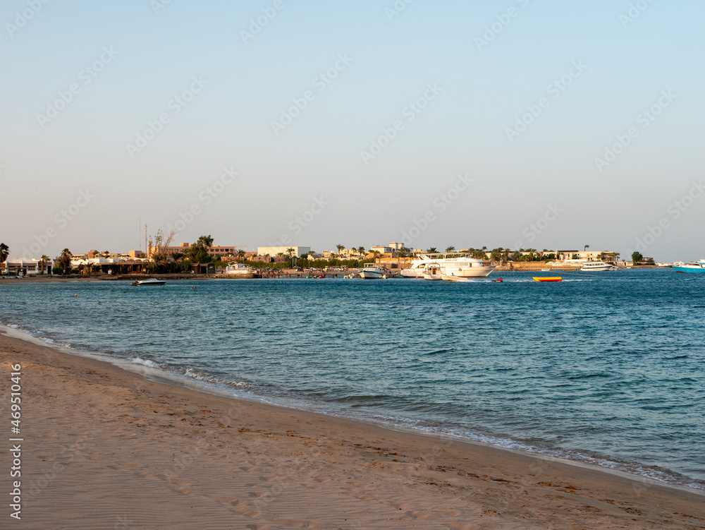 Hurghada, Egypt - September 22, 2021: Sandy beach of the red sea at sunset. Yachts and boats stand near the pier, tourists return from a sea excursion. Copy space.